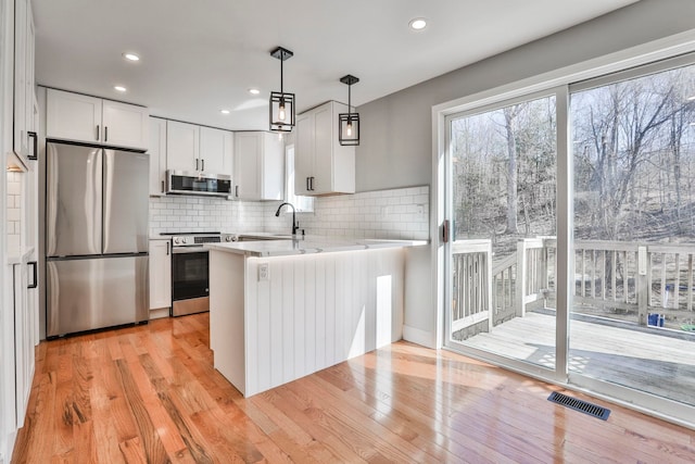 kitchen featuring light wood-type flooring, visible vents, appliances with stainless steel finishes, a peninsula, and white cabinets