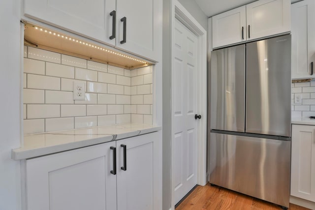 kitchen featuring white cabinetry, decorative backsplash, light wood-style floors, and freestanding refrigerator