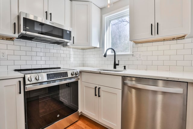 kitchen featuring a sink, stainless steel appliances, decorative backsplash, and white cabinetry