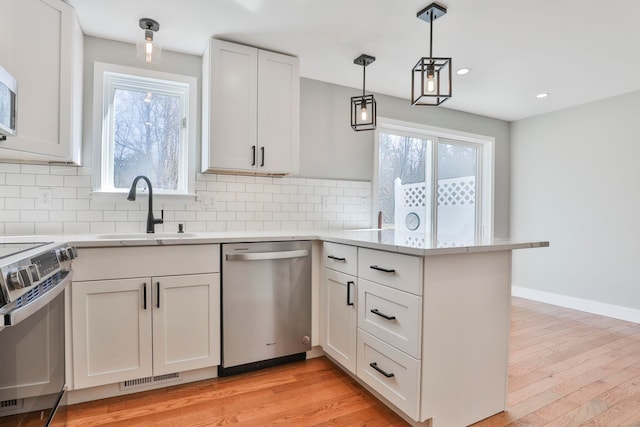 kitchen with decorative backsplash, light wood-style flooring, a peninsula, stainless steel appliances, and a sink