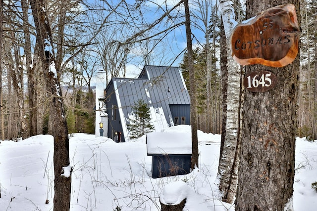 snow covered property with a standing seam roof, a gambrel roof, metal roof, and a garage