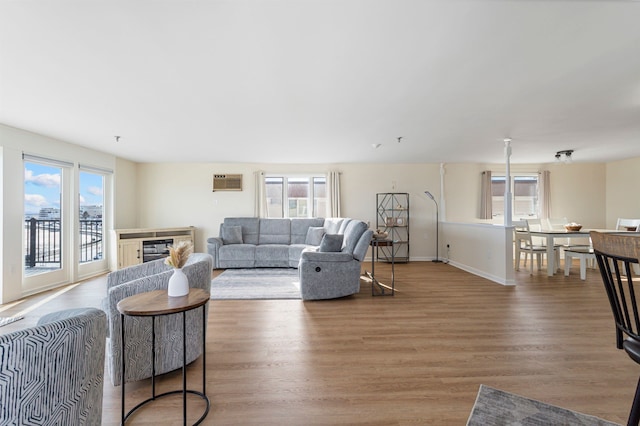 living room with a wall mounted air conditioner, baseboards, and light wood-style floors