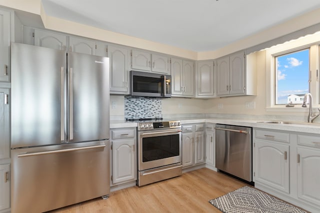 kitchen featuring light wood-type flooring, a sink, stainless steel appliances, light countertops, and tasteful backsplash