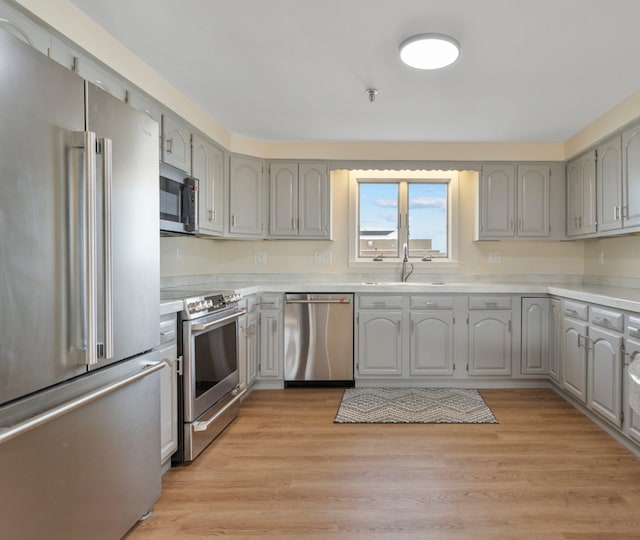 kitchen featuring light wood-style flooring, gray cabinetry, stainless steel appliances, and a sink