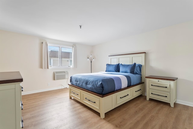 bedroom featuring light wood finished floors, baseboards, and a wall unit AC