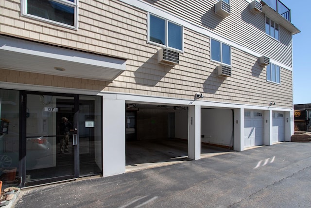 exterior space with an attached garage and a wall mounted air conditioner