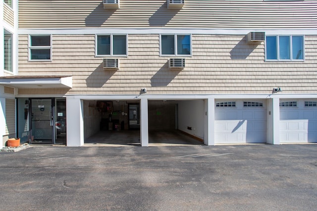 rear view of house with an AC wall unit, a garage, and driveway