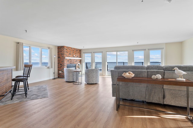 living room featuring baseboards, a brick fireplace, a healthy amount of sunlight, and wood finished floors