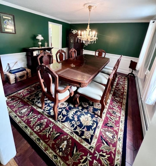 dining area with wood finished floors, a wainscoted wall, ornamental molding, a baseboard heating unit, and a chandelier