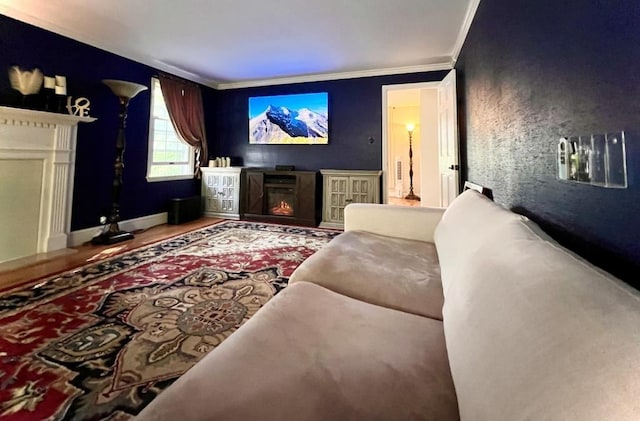 home theater featuring baseboards, wood finished floors, a glass covered fireplace, and ornamental molding