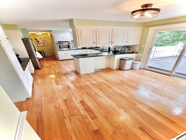 kitchen with dark countertops, a peninsula, light wood-style flooring, white cabinets, and stainless steel oven