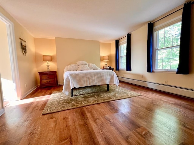 bedroom featuring a baseboard radiator, baseboards, and wood finished floors