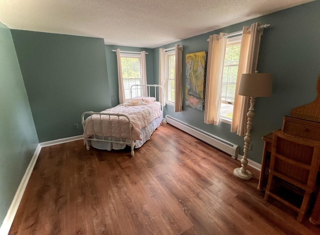 bedroom featuring multiple windows, baseboard heating, wood finished floors, and a textured ceiling