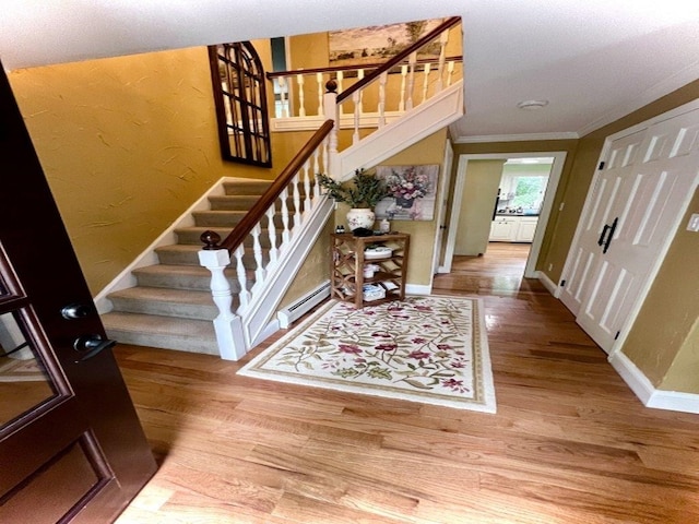 foyer entrance featuring stairs, a baseboard heating unit, baseboards, and wood finished floors