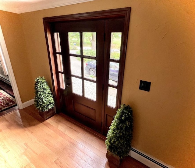 foyer entrance featuring baseboards, baseboard heating, a healthy amount of sunlight, and light wood finished floors