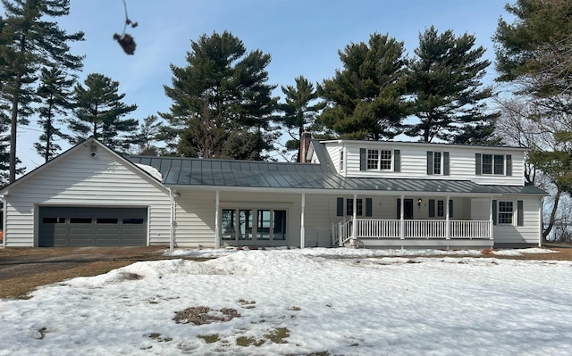 view of front facade featuring covered porch, a chimney, metal roof, a garage, and a standing seam roof