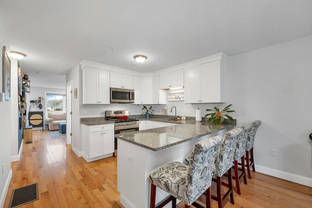 kitchen featuring stainless steel appliances, white cabinetry, visible vents, and light wood finished floors