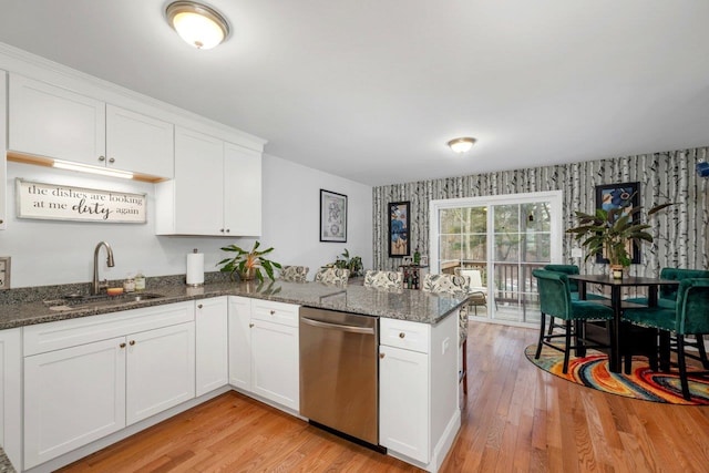 kitchen with a sink, stainless steel dishwasher, a peninsula, white cabinets, and wallpapered walls