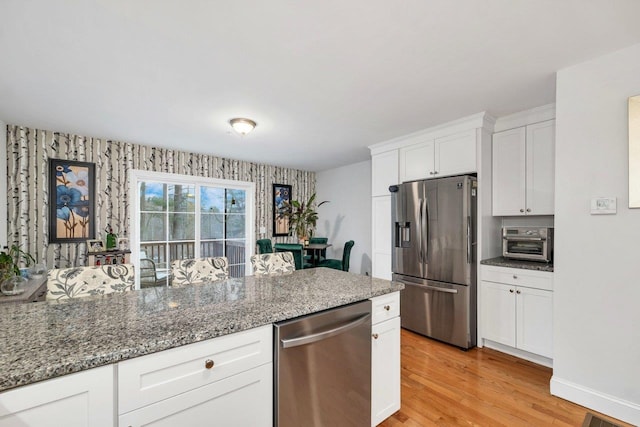 kitchen featuring light wood-type flooring, white cabinetry, stainless steel appliances, stone counters, and baseboards