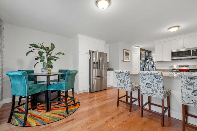 kitchen featuring a breakfast bar area, light stone countertops, appliances with stainless steel finishes, white cabinetry, and light wood-type flooring