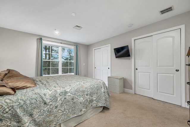 bedroom featuring visible vents, light colored carpet, two closets, and baseboards