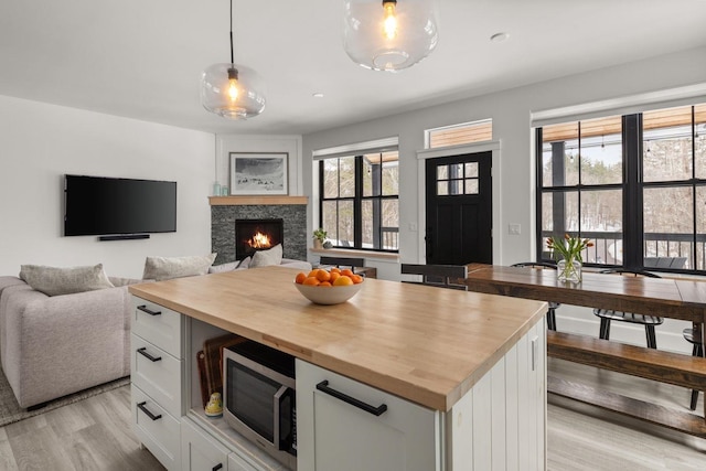 kitchen with wooden counters, light wood-style flooring, a warm lit fireplace, white cabinets, and stainless steel microwave