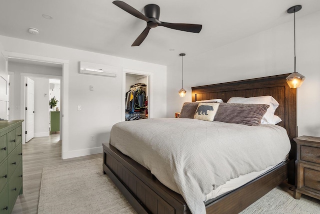 bedroom with an AC wall unit, light wood-style floors, baseboards, ceiling fan, and a spacious closet