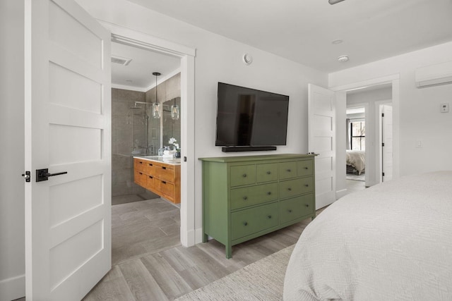 bedroom with ensuite bath, a wall unit AC, visible vents, and light wood finished floors