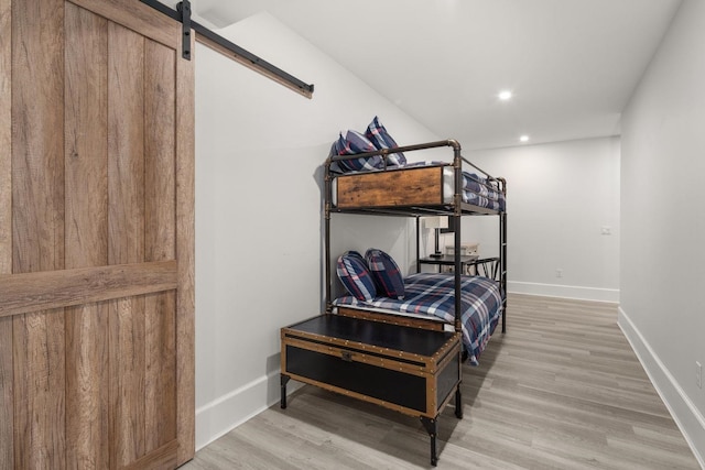 bedroom featuring recessed lighting, a barn door, baseboards, and light wood-style flooring