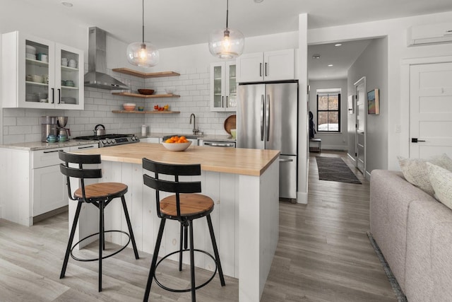 kitchen with wooden counters, wall chimney range hood, decorative backsplash, a kitchen breakfast bar, and freestanding refrigerator