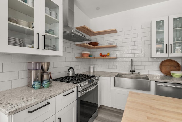 kitchen with a sink, wood finished floors, white cabinetry, stainless steel appliances, and wall chimney range hood