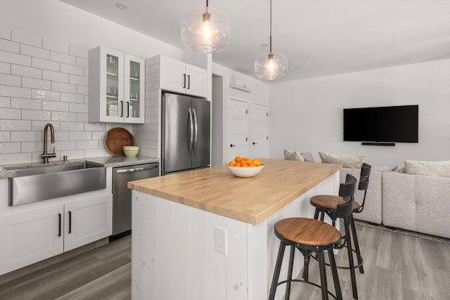 kitchen with wood finished floors, a sink, decorative backsplash, stainless steel appliances, and a kitchen breakfast bar