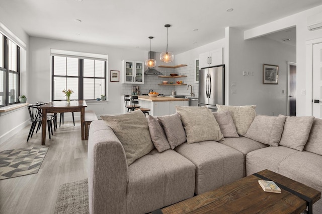 living area featuring plenty of natural light, a wall mounted AC, light wood-type flooring, and baseboards