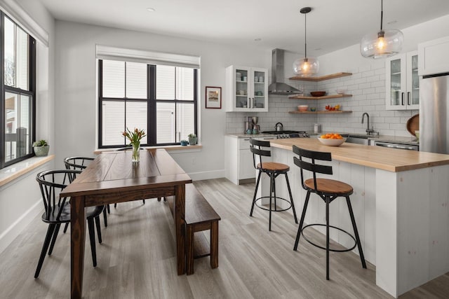 kitchen with a kitchen island, wood counters, a kitchen bar, decorative backsplash, and wall chimney exhaust hood