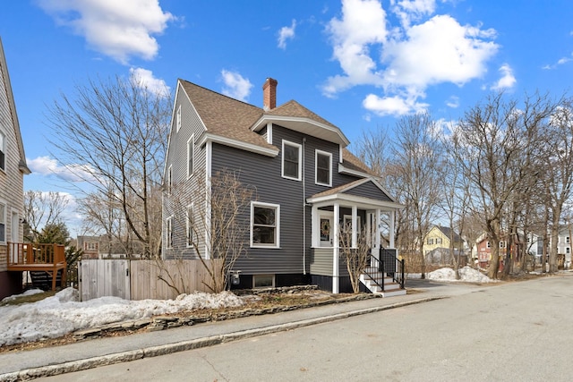 view of front of home with a shingled roof, a chimney, a residential view, and fence