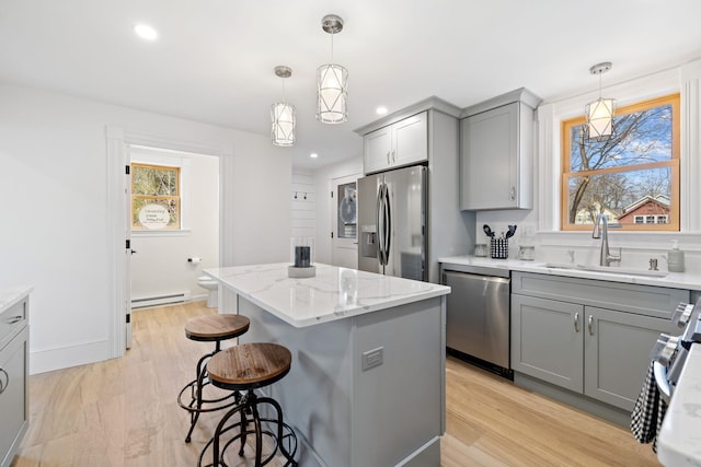 kitchen with gray cabinetry, a breakfast bar area, baseboard heating, appliances with stainless steel finishes, and a sink