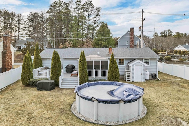 rear view of property with a covered pool, a fenced backyard, a yard, and a deck