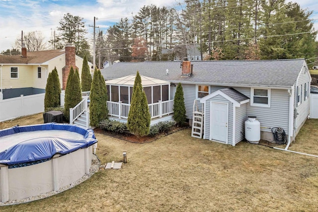 rear view of house featuring a covered pool, a yard, an outdoor structure, a sunroom, and a chimney