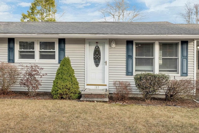 doorway to property featuring a lawn and roof with shingles