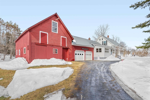 view of front of home with an outbuilding, driveway, an attached garage, a chimney, and a barn