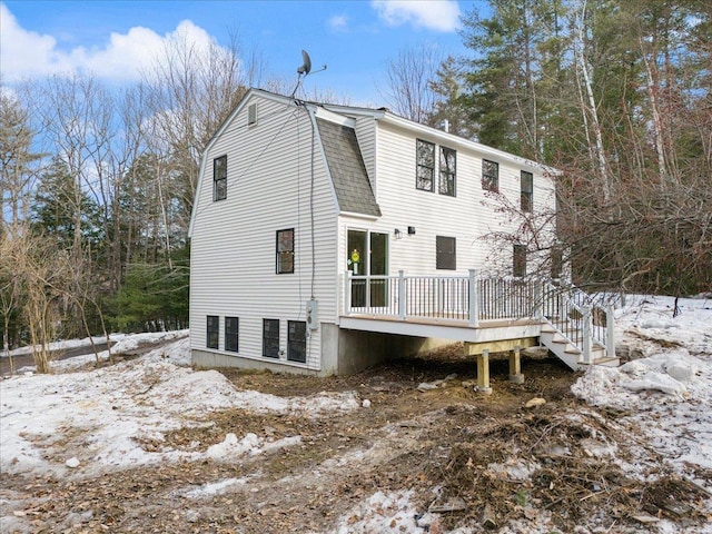 snow covered rear of property with a gambrel roof, a deck, and a shingled roof