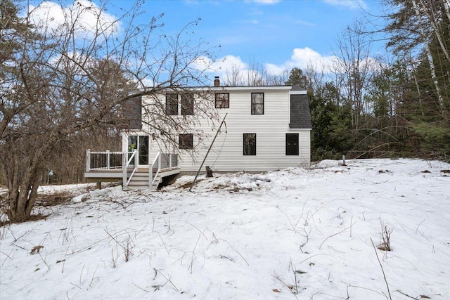 snow covered rear of property with a deck, a shingled roof, and a chimney