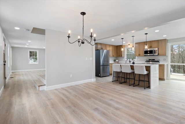 kitchen with baseboards, open floor plan, light wood-style flooring, appliances with stainless steel finishes, and a sink