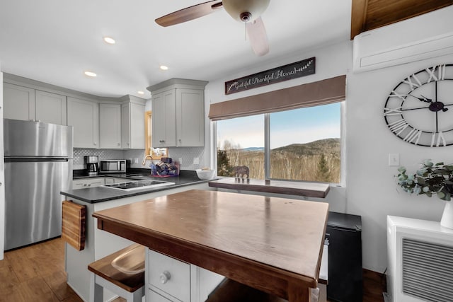 kitchen with wood finished floors, gray cabinets, stainless steel appliances, dark countertops, and backsplash