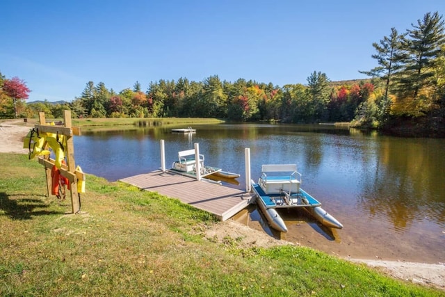 view of dock featuring a wooded view, a yard, and a water view