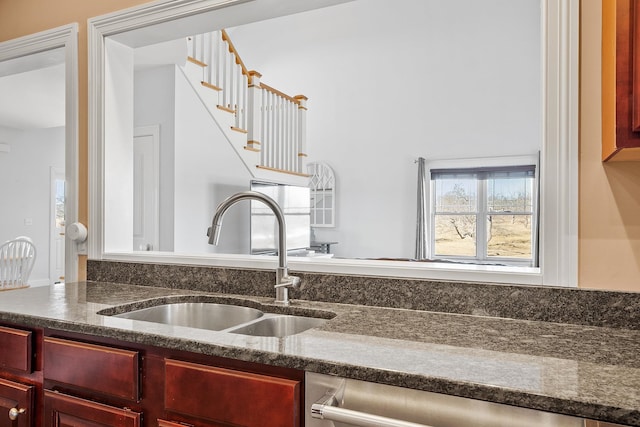 kitchen featuring a sink, dishwashing machine, reddish brown cabinets, and dark stone countertops