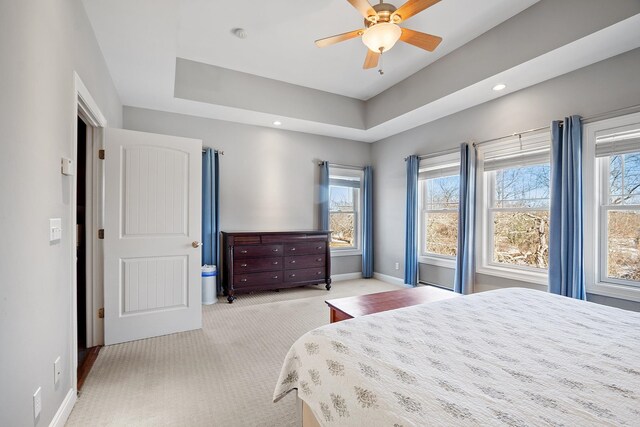 bedroom with ceiling fan, a tray ceiling, baseboards, and light carpet