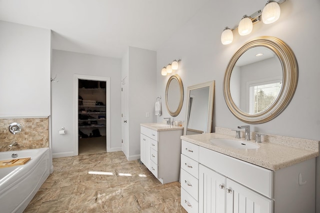 full bathroom featuring a bath, a walk in closet, two vanities, and a sink