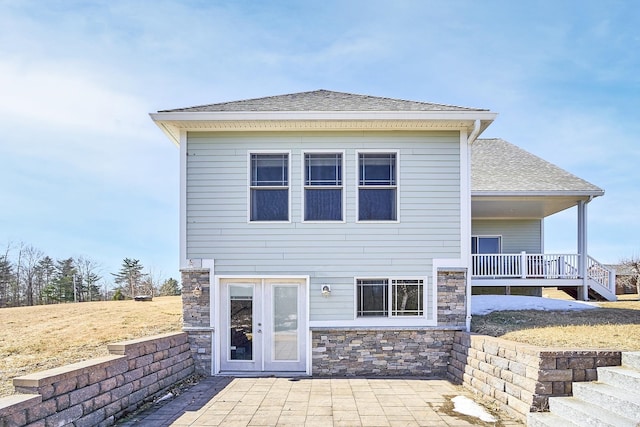 back of house featuring a patio area, stone siding, and a shingled roof