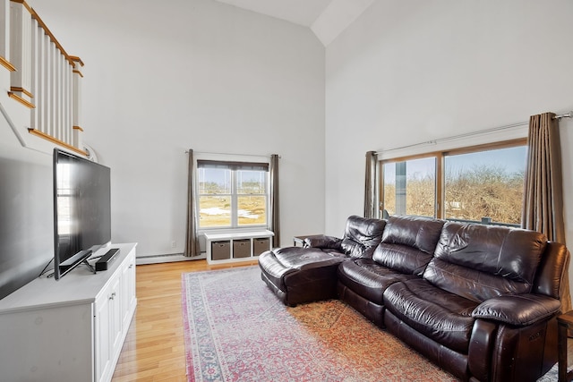 living room featuring a high ceiling, light wood finished floors, and a baseboard radiator